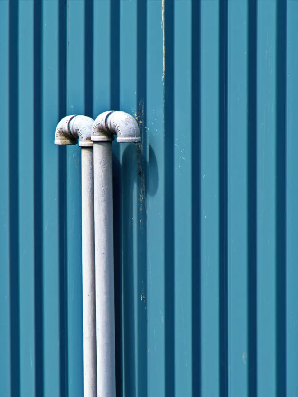White pipes running up a blue corrugated wall